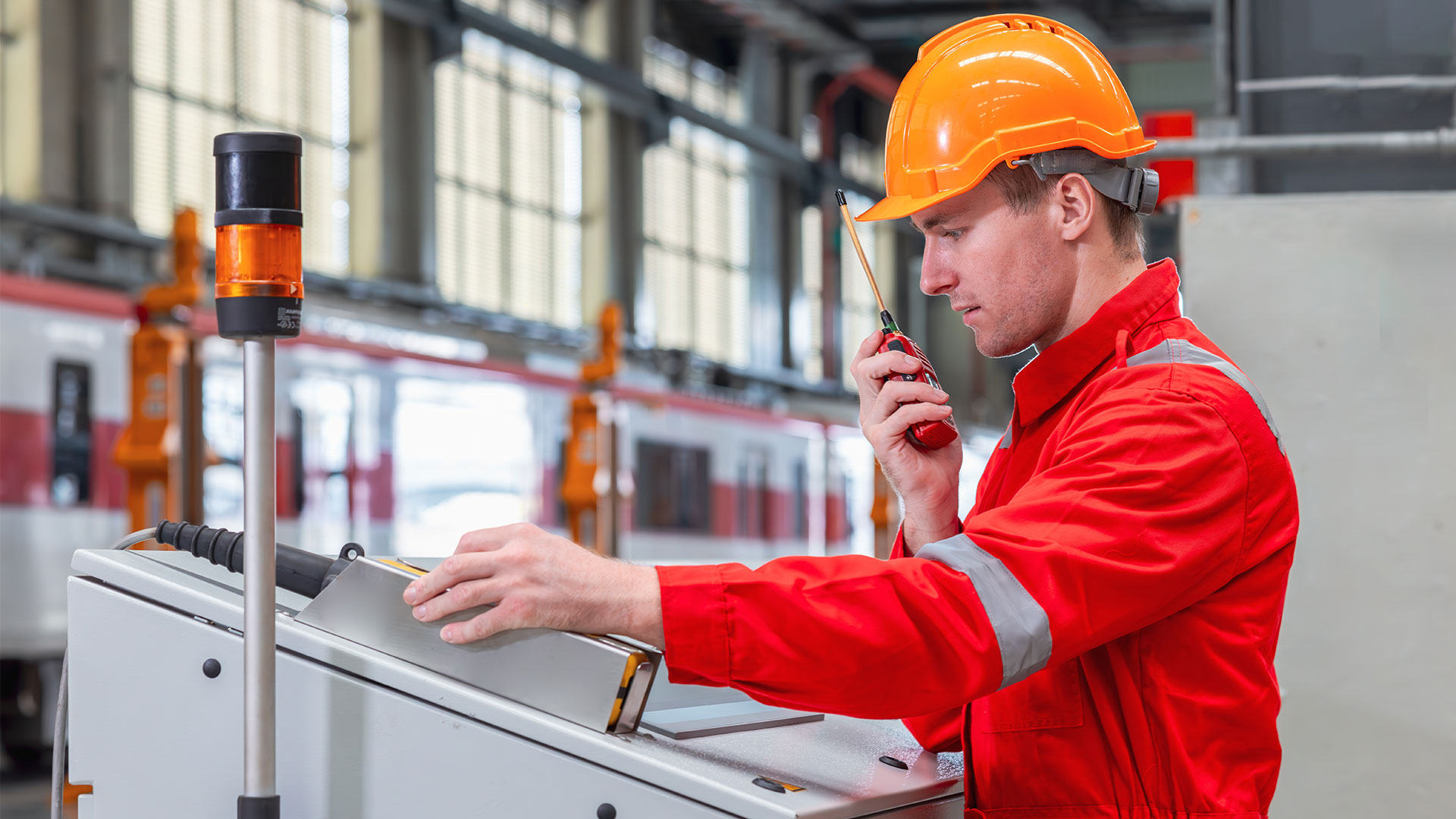 Railway technician in safety gear operating a control panel with a high-speed train in the background.